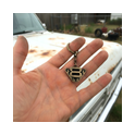 Hand hält einen Messing‑V8 Schlüsselanhänger im Flammen‑Design vor weißem amerikanischem Pickup – ideal für Muscle‑Car‑Fans, Gearheads, US‑Car‑Liebhaber und Hot‑Rod‑Freunde.