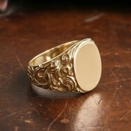 Handgefertigter barocker Siegelring aus 585 Gold mit ovaler Ringplatte und ornamentiertem Ringschaft auf Holzuntergrund
