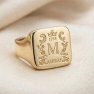 Personalisierter goldener Siegelring mit Monogramm, Wappenornamenten und individueller Gravur auf hellem Stoff