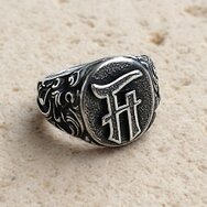 Handgefertigter Siegelring aus oxidiertem 925 Sterling Silber mit Monogramm und ornamentiertem Ringschaft auf hellem Stein