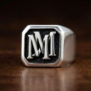 Handgefertigter Monogramm Siegelring aus 925 Sterling Silber mit erhabenen Initialen MM und geschwärztem Hintergrund auf Holzuntergrund