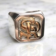 Handgefertigter Monogramm Siegelring aus 750 Gold mit erhabenen Initialen SR und strukturierter Ringplatte auf hellem Marmor