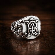 Handgefertigter Monogramm Siegelring aus 925 Sterling Silber mit erhabenen Initialen und ornamentiertem Ringschaft auf dunklem Holz