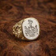 Edler Siegelring mit graviertem Familienwappen, goldener ornamentierter Ringschiene und heller Siegelplatte auf Maserholz