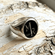 Silberner Herrenring mit schwarzem Lagenstein, eingeschnittenen Initialen und klassischer Siegelringform auf heller Birkenrinde
