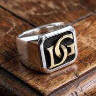 Massiver Herrenring mit silberner Ringschiene, goldenen Initialen und dunkler Siegelplatte auf rustikalem Holz