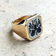 Klassischer Siegelring aus 750 Gelbgold mit hellem Lagenstein, schwarzem Familienwappen und polierter Ringschiene auf Steinuntergrund