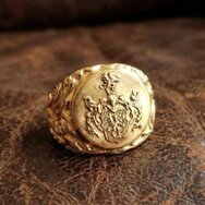 Klassischer Goldring mit graviertem Familienwappen, ornamentierter Ringschiene und warmer Präsentation auf dunklem Leder
