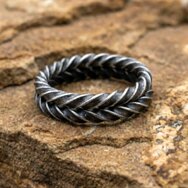 Oxidierter Silberring mit geflochtener Struktur, dunkler Patina und markanter Handarbeit auf rauem Steinuntergrund