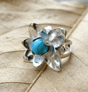 Floraler Silberring in Form einer Lotusblüte mit türkisfarbener Edelsteinperle und glänzenden Blütenblättern auf hellem Naturblatt