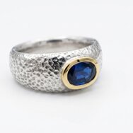 Breiter Bandring aus Silber mit Hammerschlag-Optik und einem in 750er Gold gefaßtem blauen Saphir