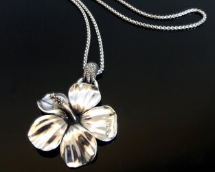 Fertiger handgefertigter Anhänger einer Hibiskusblüte, die von einer detaillierten Chamäleonhand umschlossen wird, glänzend poliert