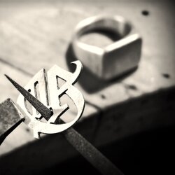 Nahaufnahme eines von Hand ausgesägten Monogramms aus Metall in der Nachbearbeitung, bereit zum Löten auf einen Siegelring