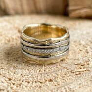 Ein breiter Ring mit organischer Wellenform, weißgold-farbenen Streifen und eingefassten Diamanten.